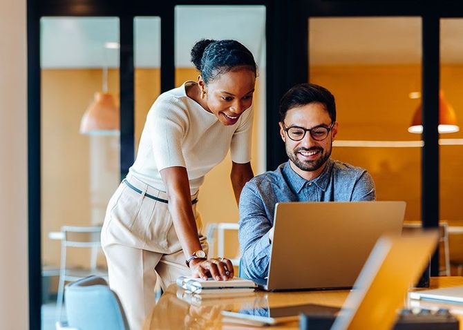 Two coworkers smiling and collaborating at a laptop in a modern office