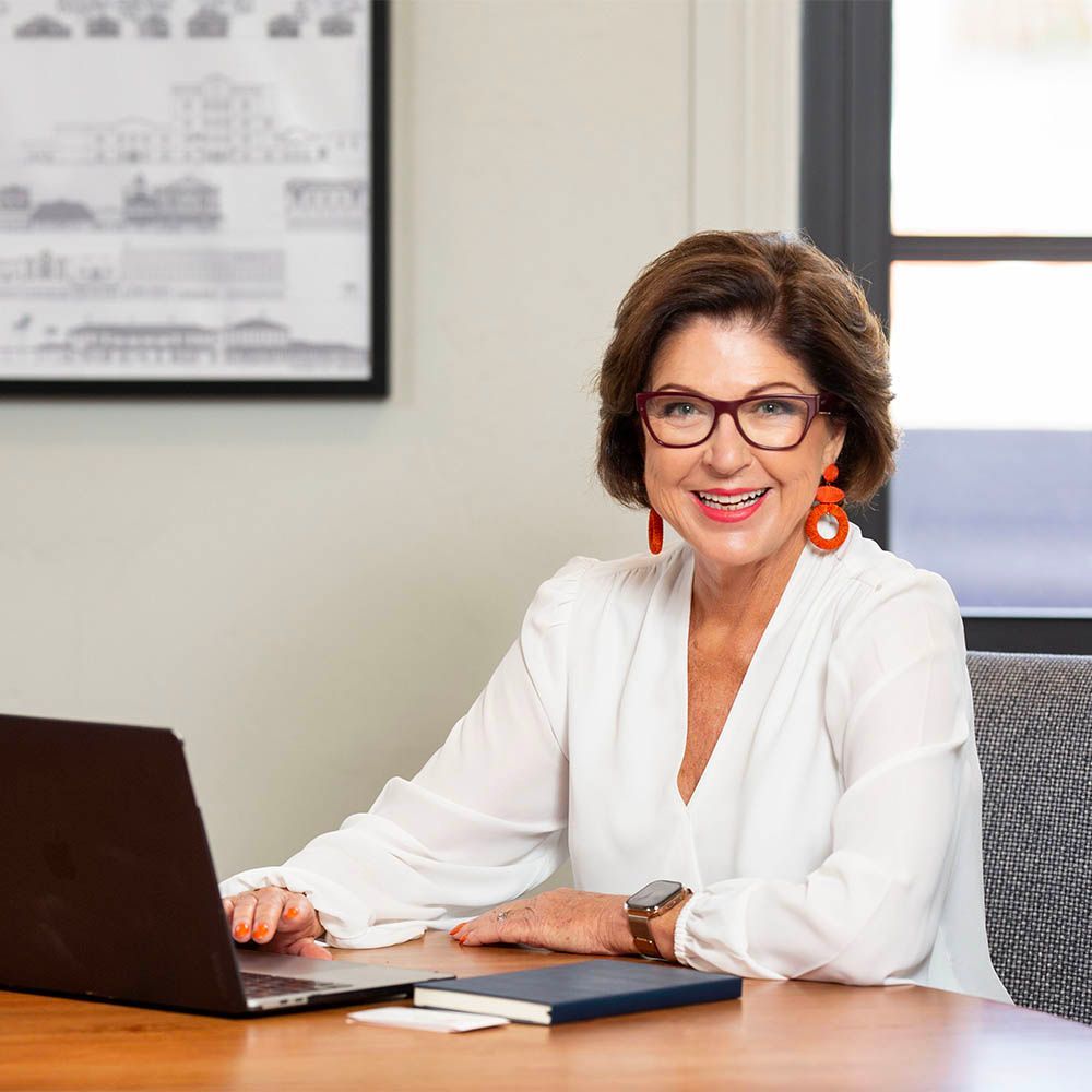 Smiling woman with glasses working at a desk with a laptop in a bright office