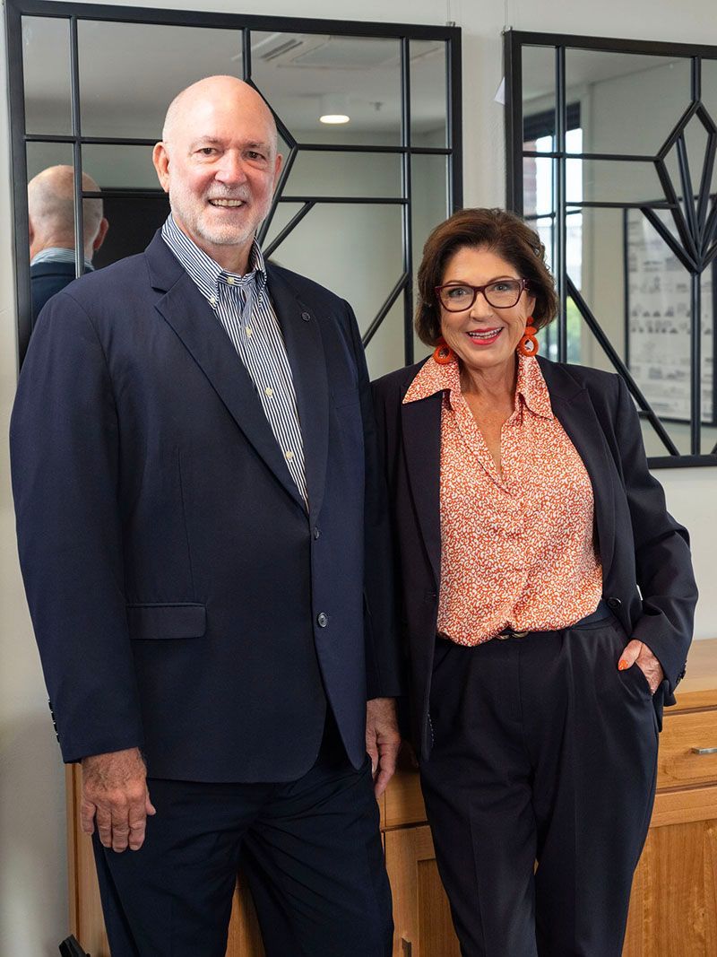 Two people smiling indoors, standing in front of a geometric mirror wall.