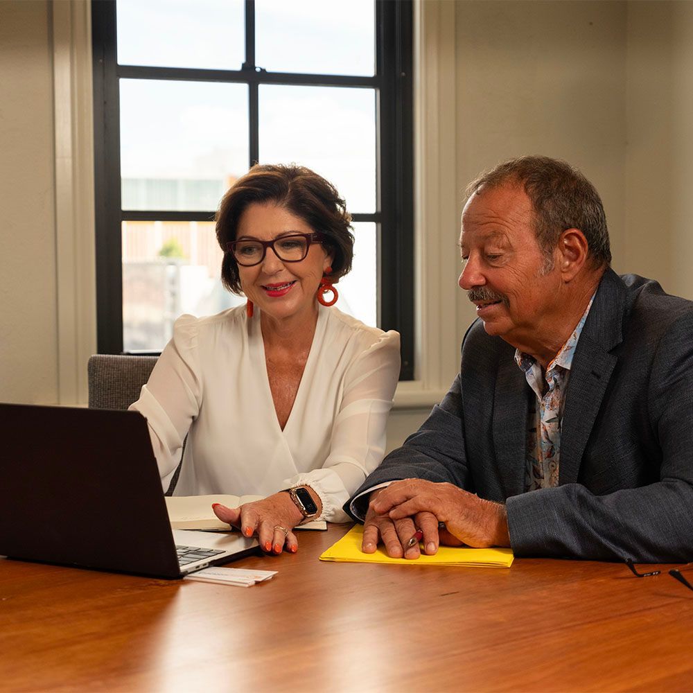Two colleagues smiling at a laptop on a conference table in a bright office