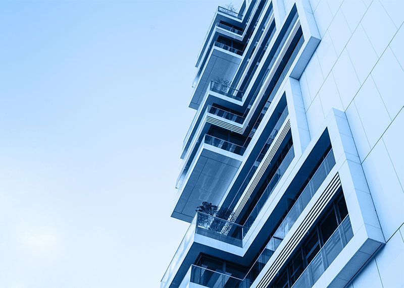 Modern glass high-rise viewed from below against a pale blue sky