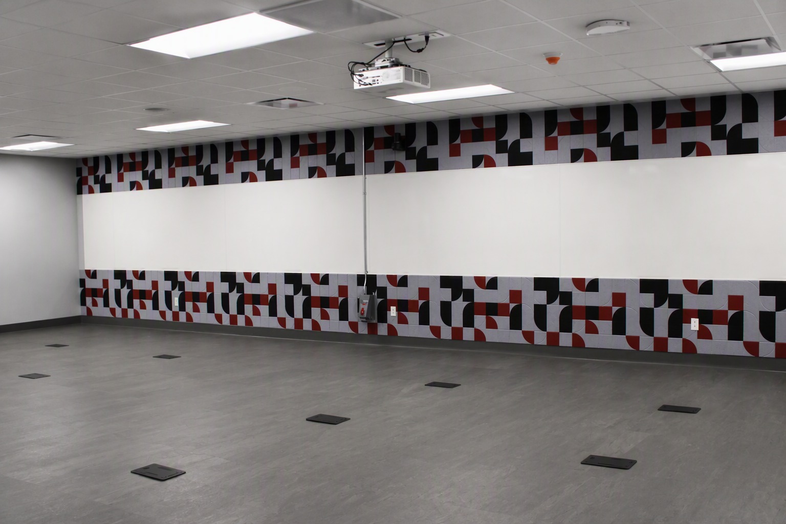 Empty classroom with whiteboards, patterned wall border, and gray tiled floor.