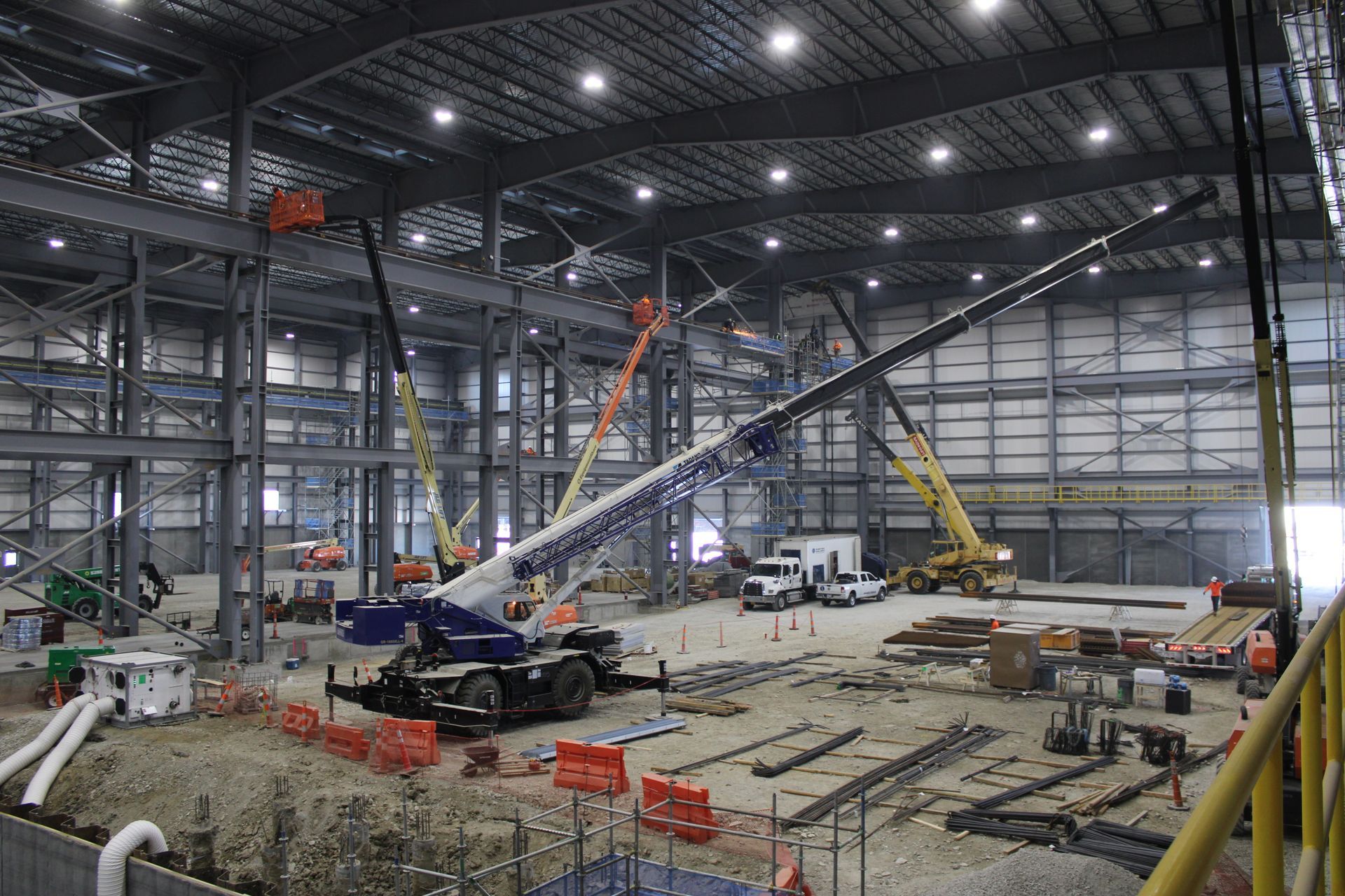 Large indoor construction site with cranes, scaffolding, and workers beneath a high steel roof
