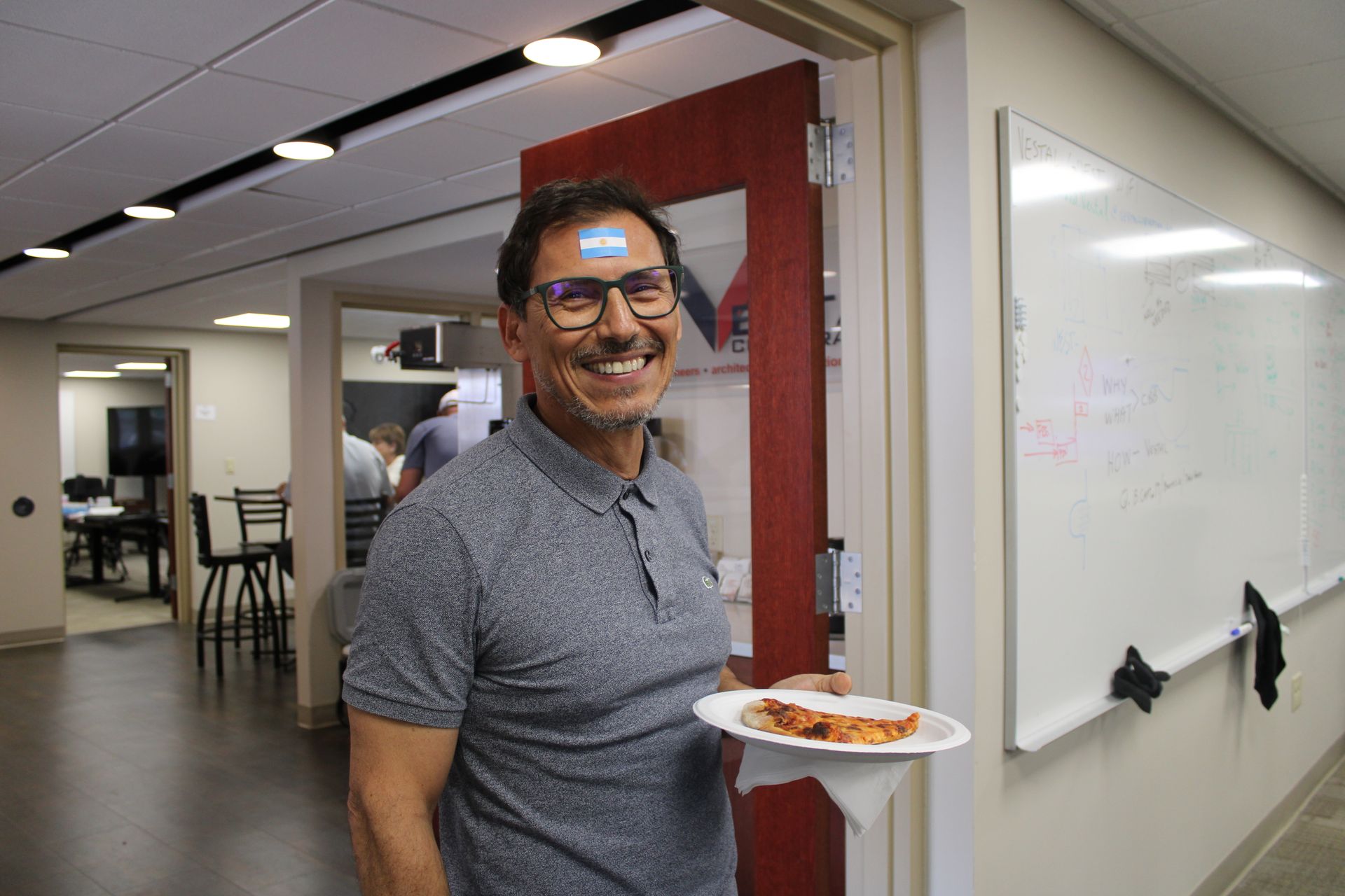 man smiling in an office area with a slice of pizza 
