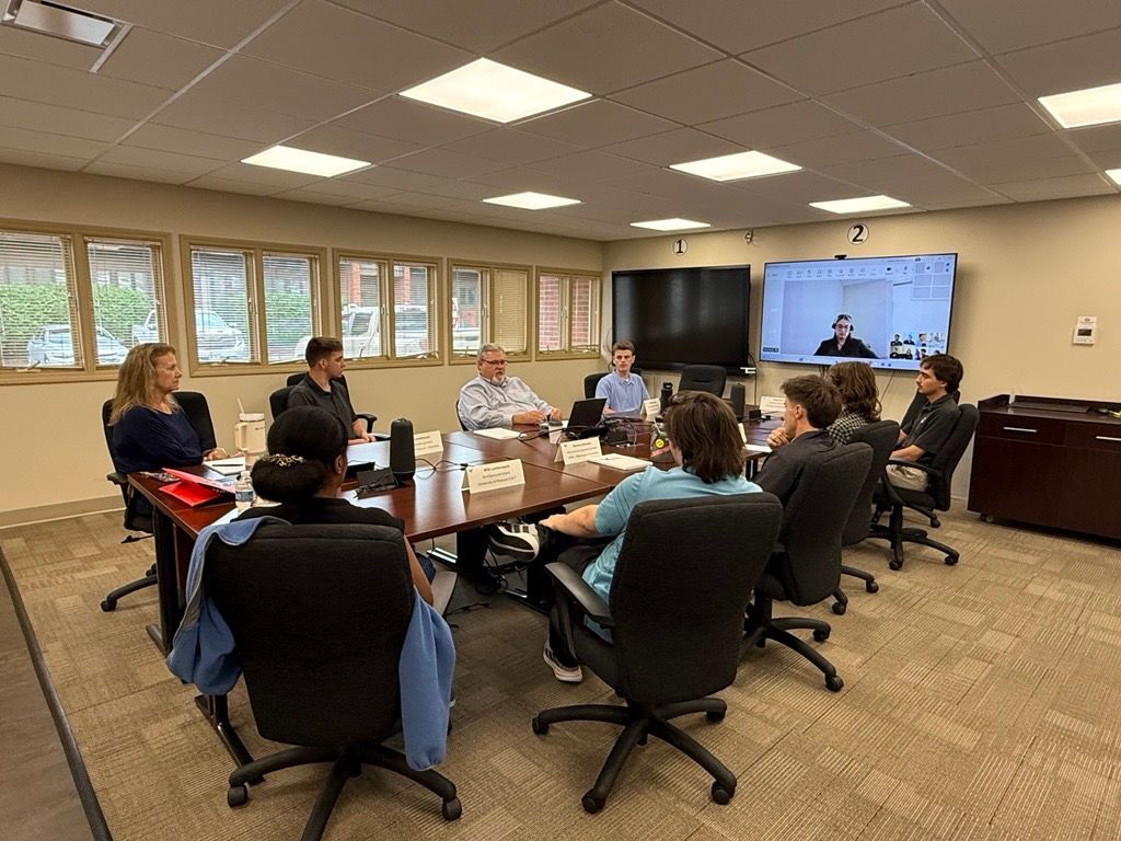 People seated around a conference table in a meeting room with a large display screen.