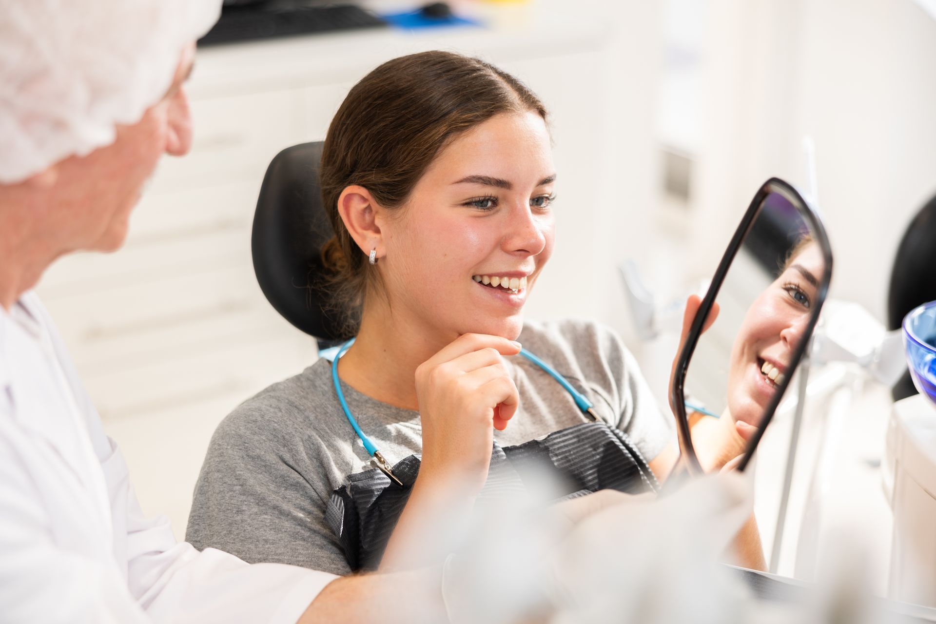 Smiling woman looks at her new smile in a handheld mirror during a dental visit