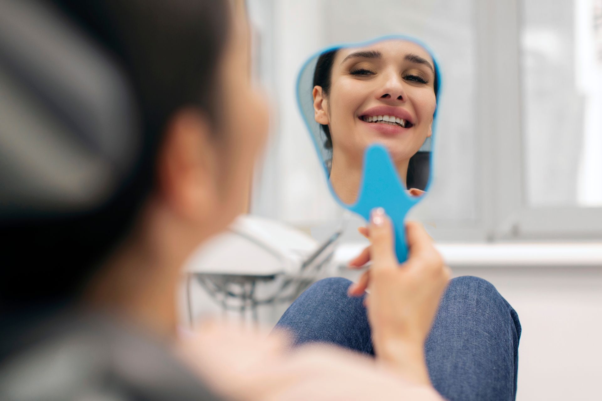 Person examines their face in a mirror with a blue facial tool in a bright room