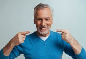 Man smiling and pointing to his nice teeth due to dental crown in Denver