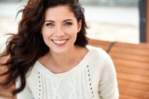 Beautiful woman with curly hair in a sweater shows off her perfect smile and teeth thanks to dental bonding
