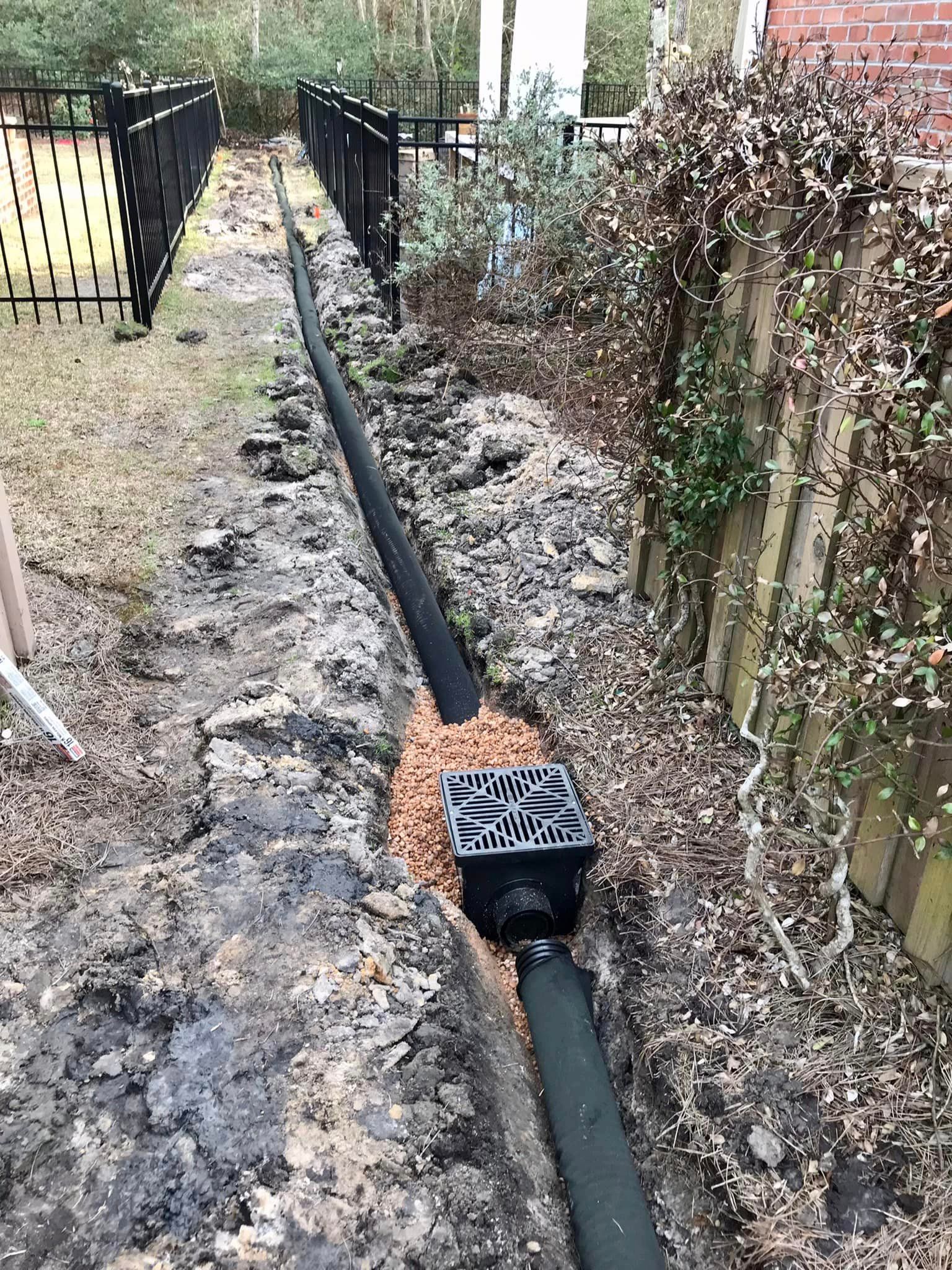 A drain pipe is being installed in a yard next to a fence.