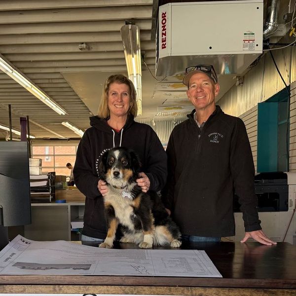 A man and woman holding a dog in front of a reznor machine