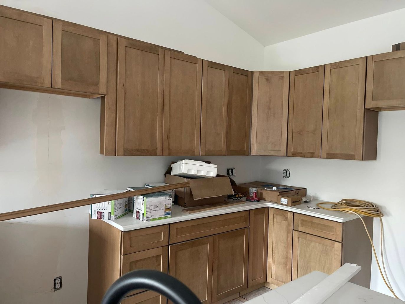 Unfinished kitchen with wooden cabinets, countertop clutter, and white walls during renovation.