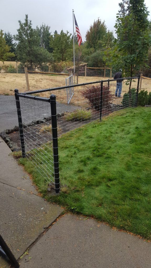 A man is standing in front of a fence with an american flag in the background.