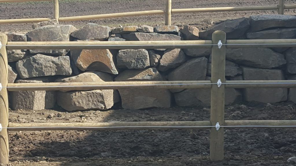 A wooden fence with a stone wall in the background