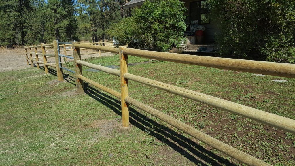 A wooden fence surrounds a grassy field in front of a house.