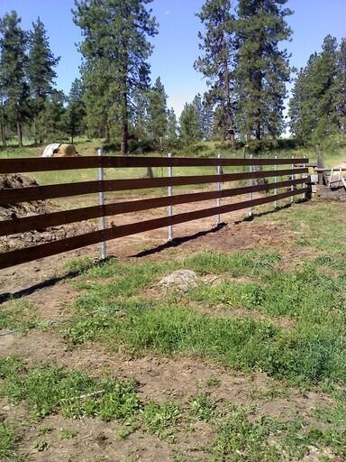 A wooden fence surrounds a grassy field with trees in the background