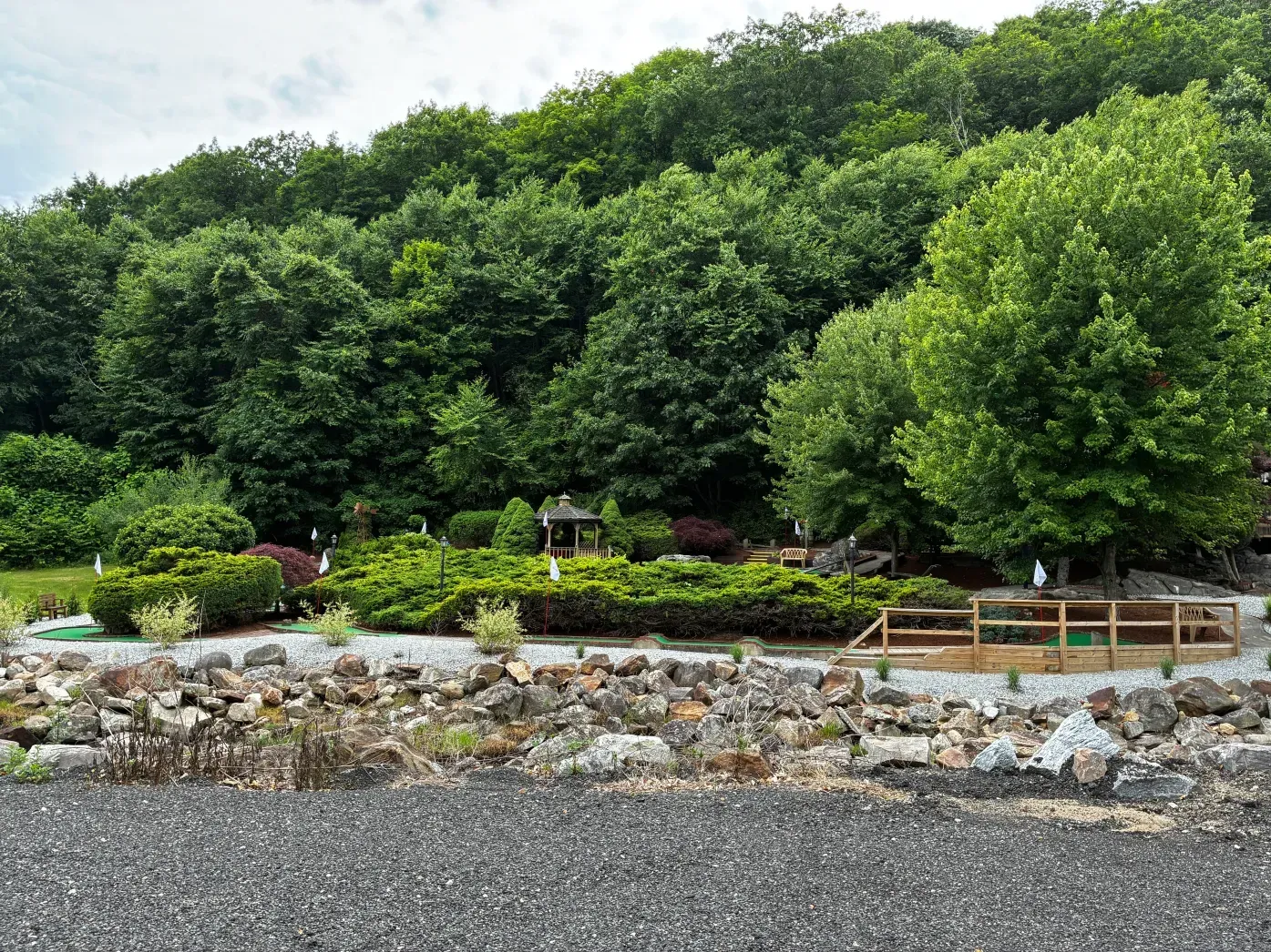 Gravel garden path beside a stone wall and lush green trees and shrubs in a park setting