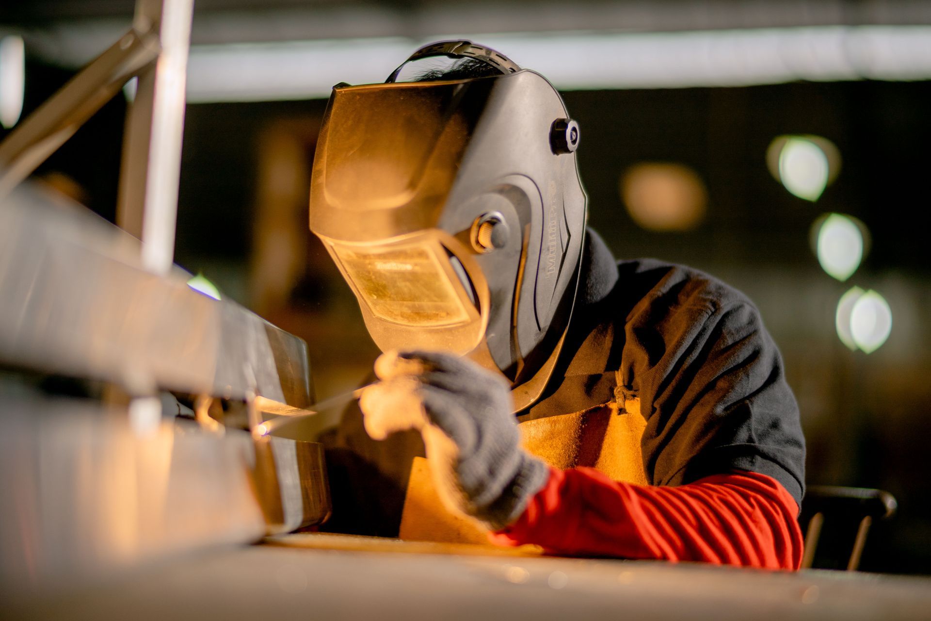 Welder in protective mask and gloves working on metal with sparks in a workshop