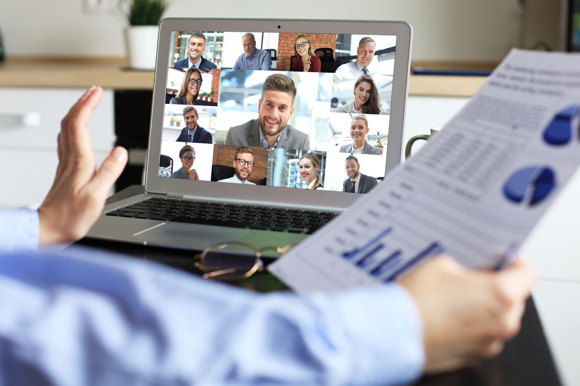 a man holds a piece of paper in front of a laptop with a group of people on it