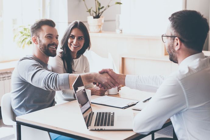 a man and woman shaking hands with a man in front of a laptop