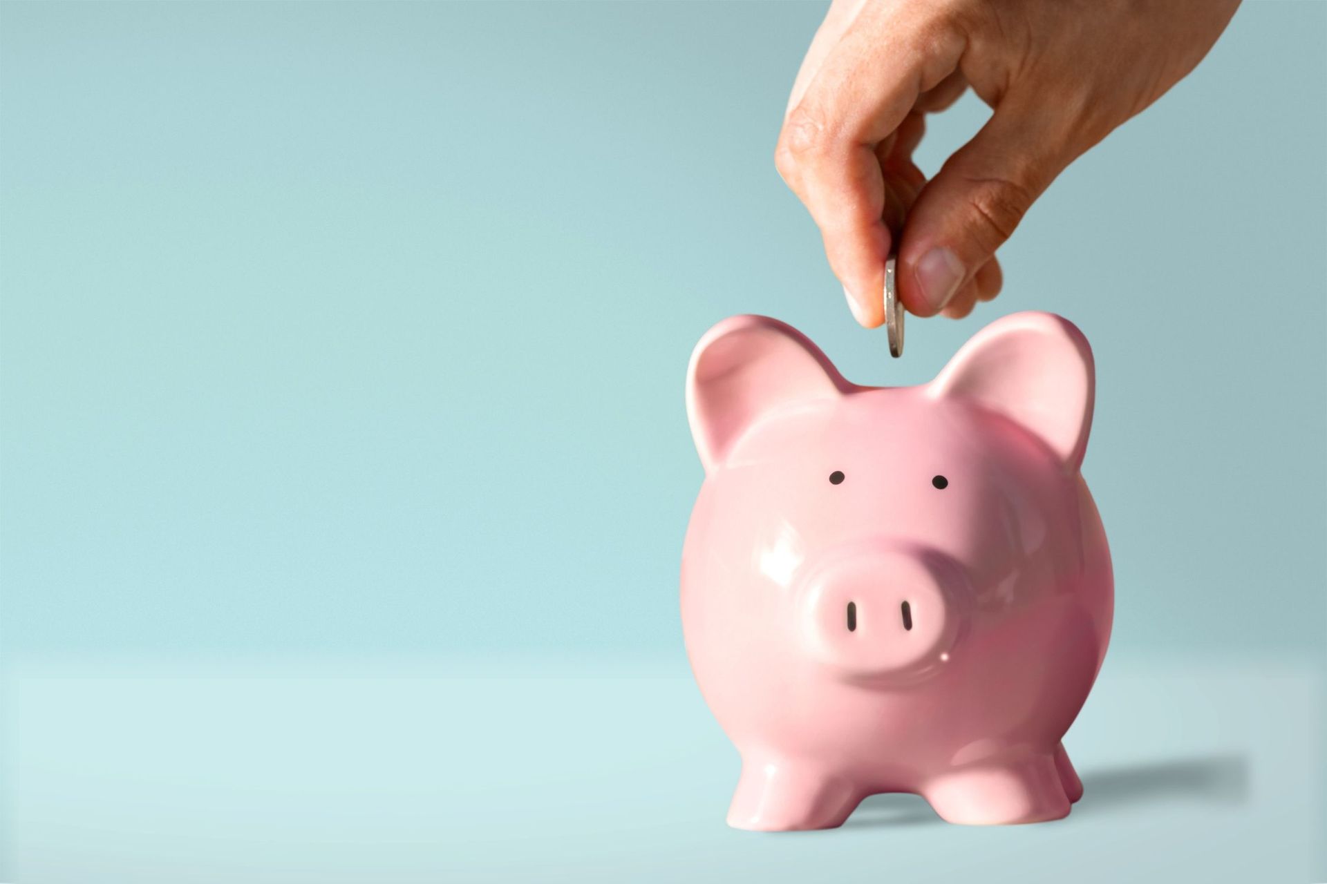 a person putting a coin into a pink piggy bank