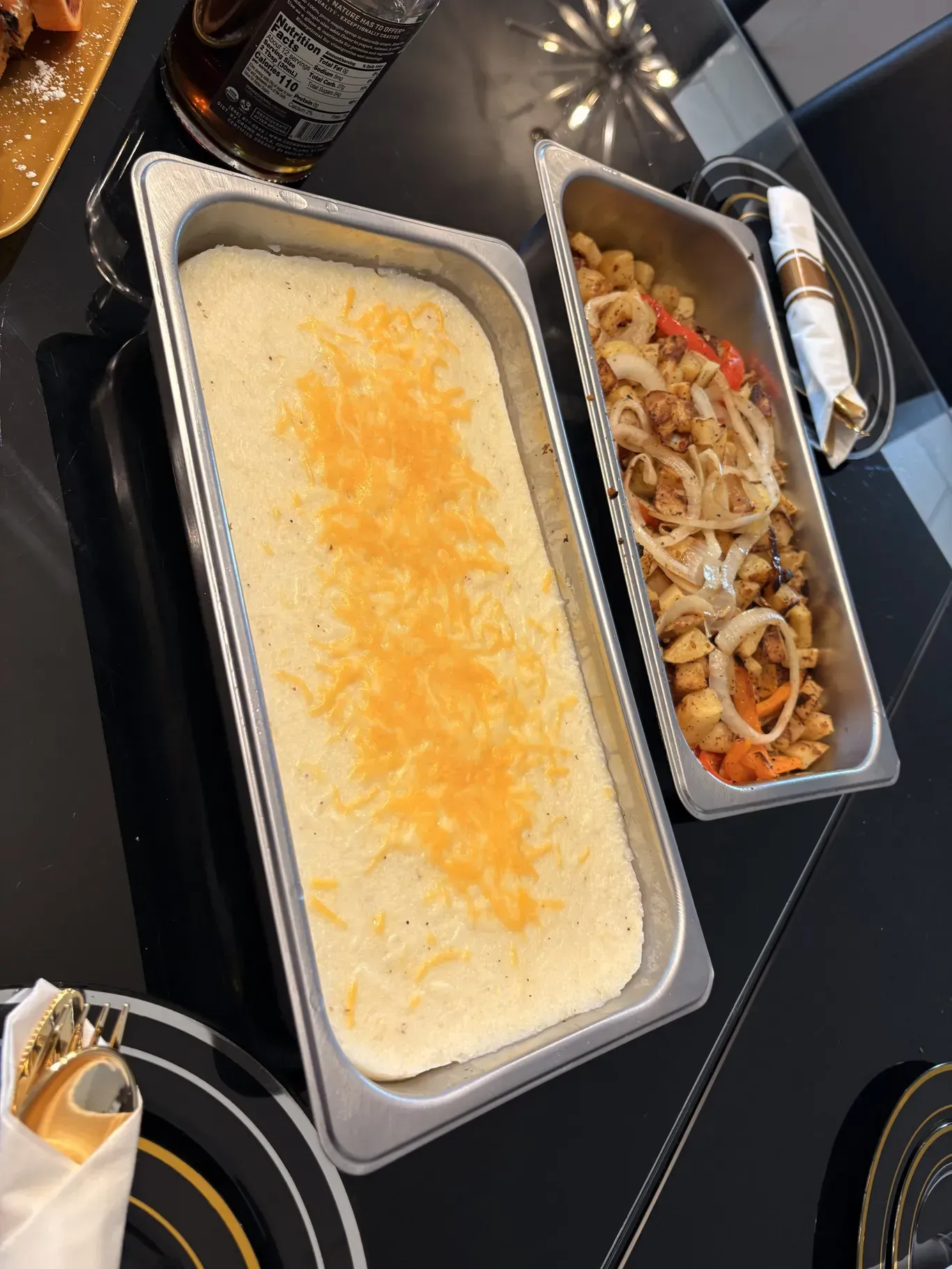 Overhead view of a dining table with a creamy baked dish and a tray of sautéed onions and peppers