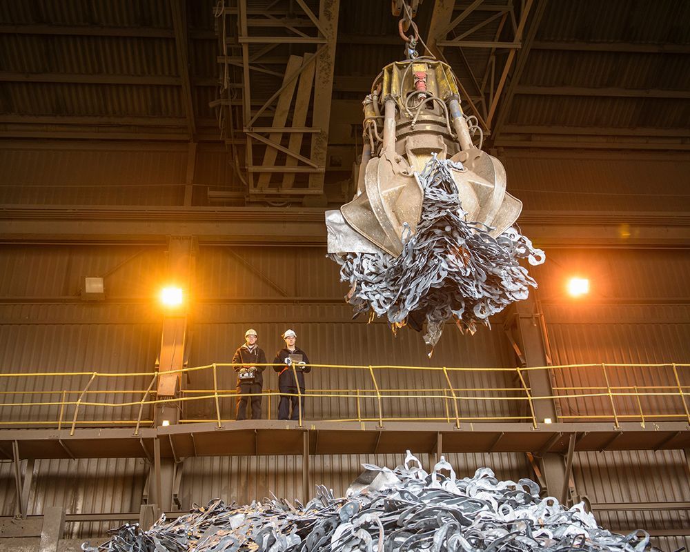 Low angle view of workers watching scrap metal grab in steel foundry, industrial machinery, teamwork, heavy industry