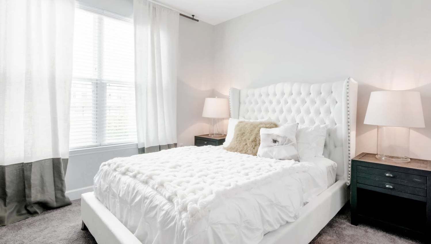 White bedroom with tufted headboard, white bedding, and two dark nightstands with lamps at Olympus Preserve at Town Center.