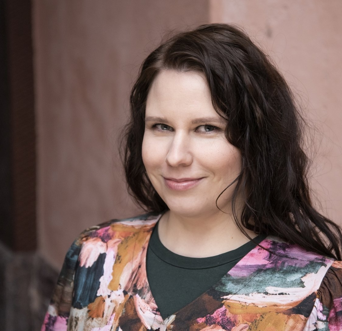 Kirjailija Helena Immonen katsoo kameraan päällään värikäs paita.
