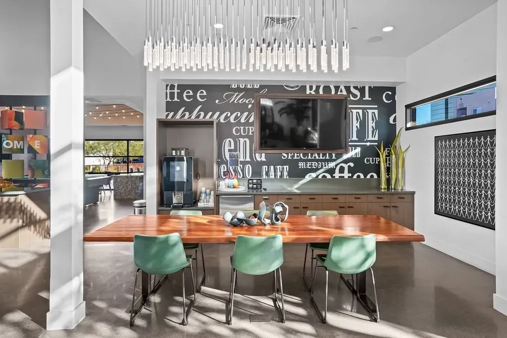 Community coffee bar with a large table, green chairs, and a TV mounted on a coffee-themed wall.