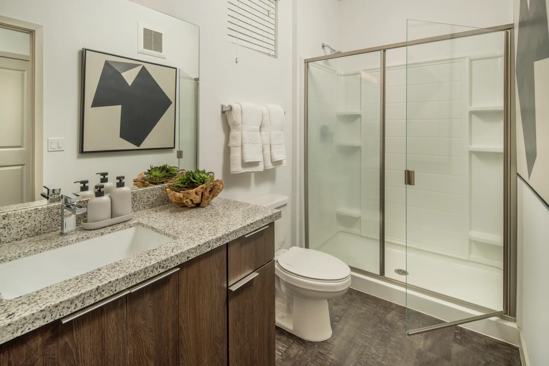 Modern bathroom with a granite countertop vanity, white sink, and glass-enclosed shower at The Landing at Fiesta Village in mesa, AZ.