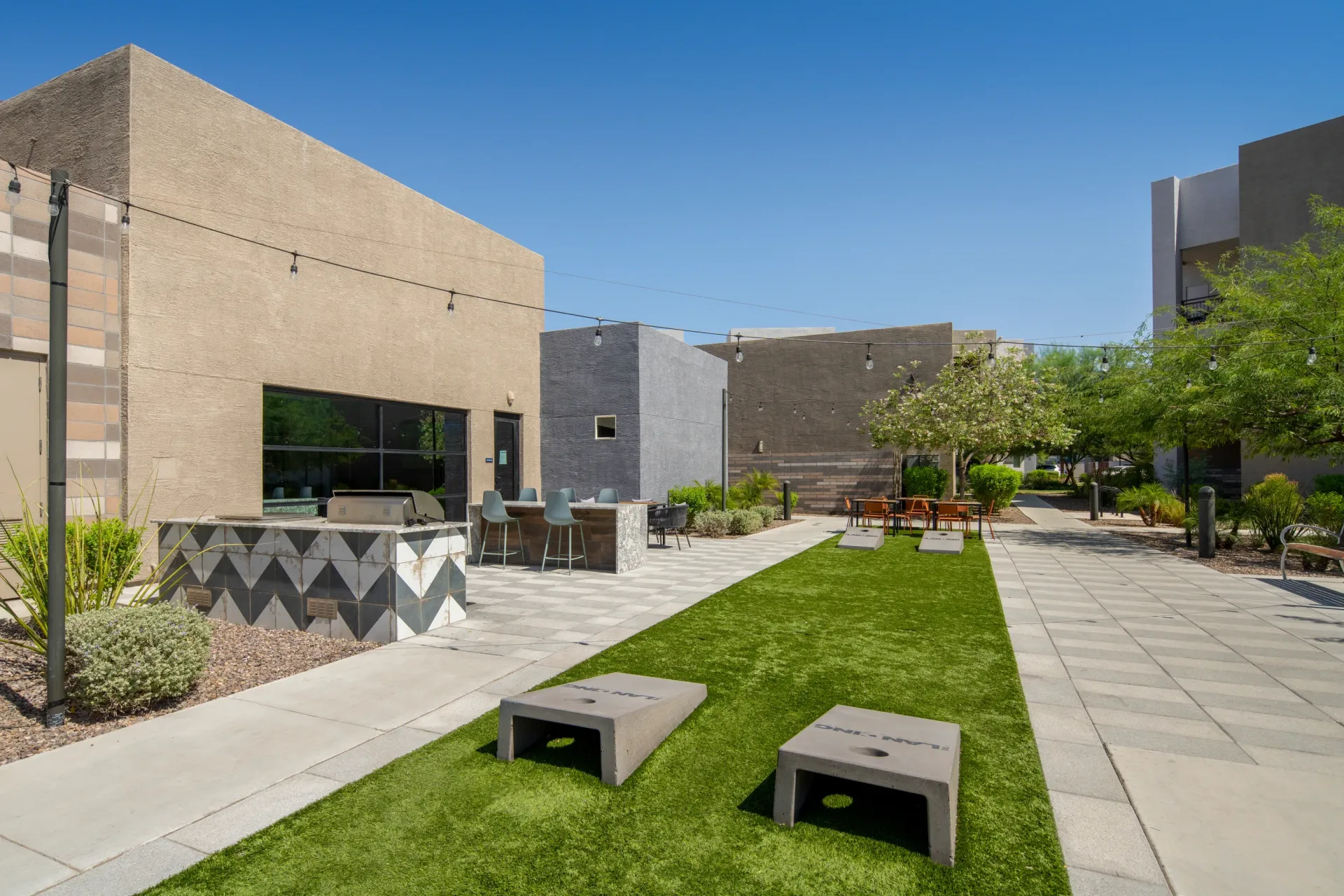 Outdoor entertainment area with a grill, bar seating, and cornhole games at The Landing at Fiesta Village in mesa, AZ.