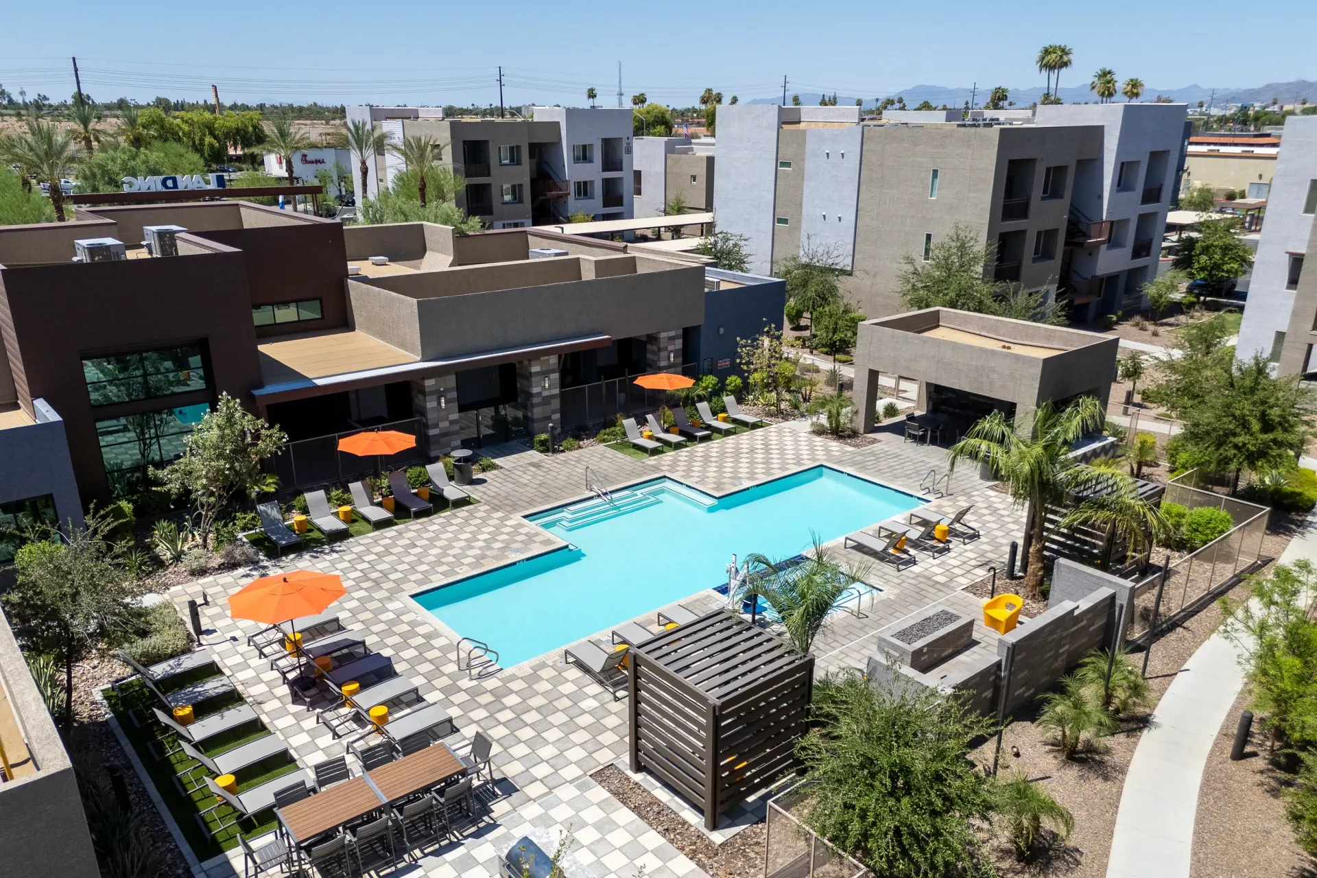 Aerial view of a modern apartment complex courtyard with a sparkling swimming pool, lounge chairs, umbrellas, and an outdoor dining area at The Landing at Fiesta Village in mesa, AZ.