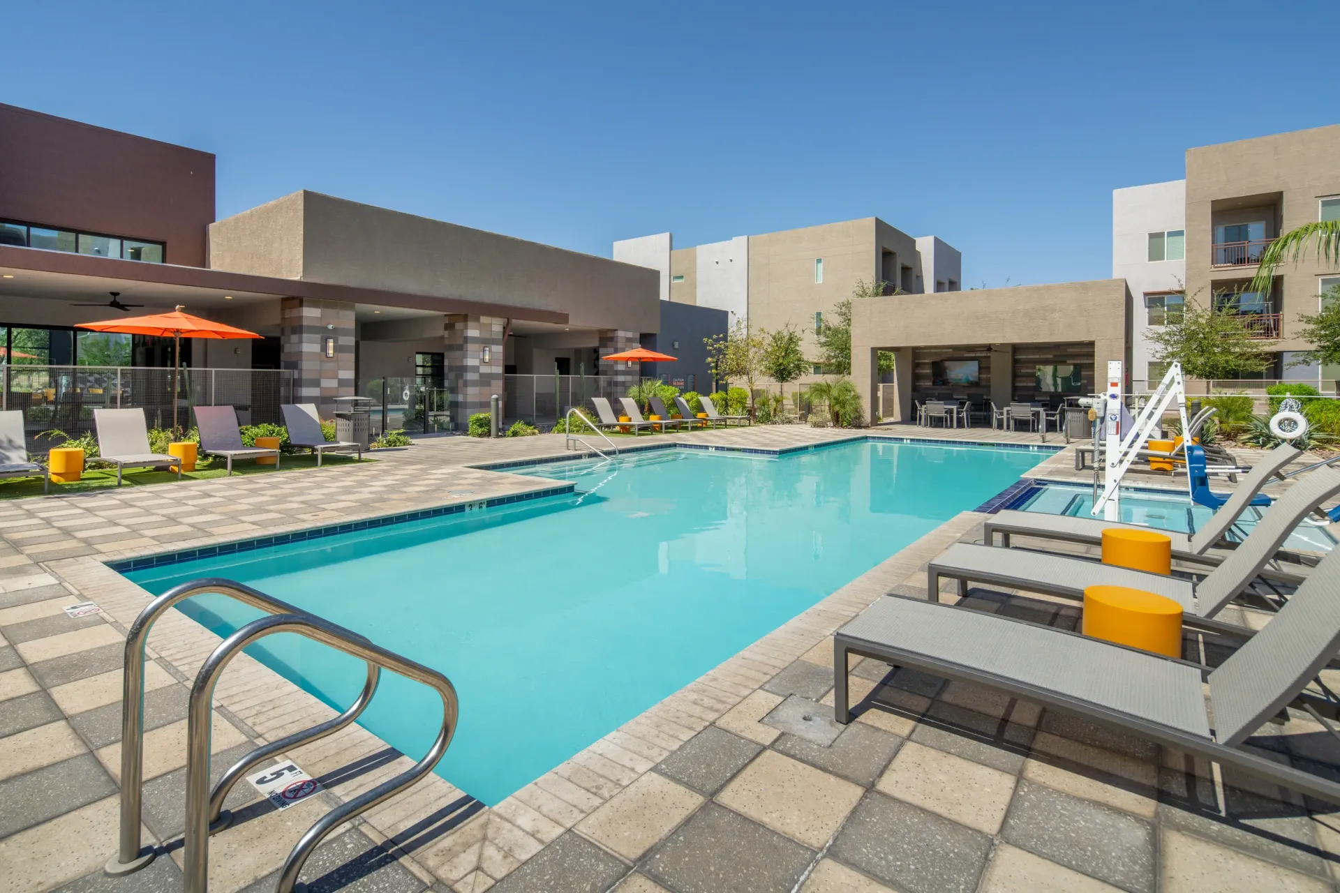 Resort-style swimming pool with lounge chairs and umbrellas at a modern apartment complex at The Landing at Fiesta Village in mesa, AZ.