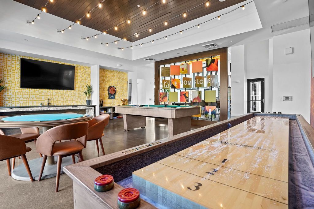 Indoor community recreation room with pool tables, lounge seating, and string lights.