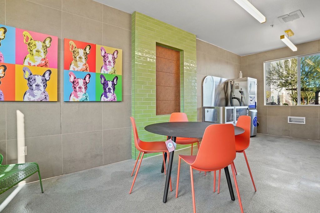Common lounge with round table, orange chairs, colorful dog-art wall, and a vending/water station.