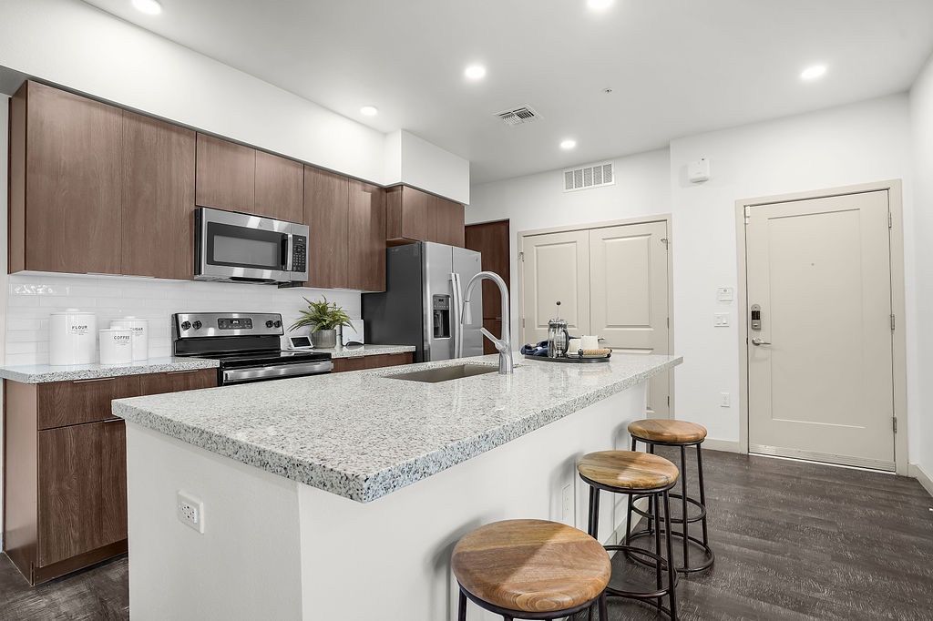 Modern kitchen with granite island, stainless-steel appliances, and three wooden bar stools.