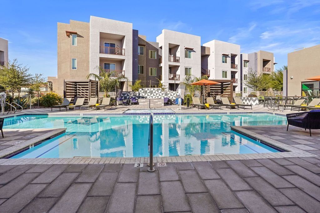 Outdoor pool area with lounge chairs and surrounding apartment buildings.