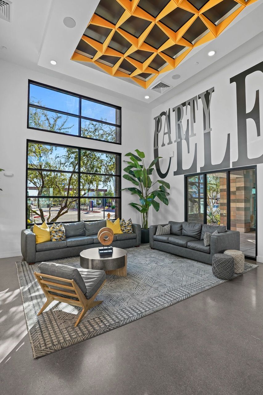 Bright modern leasing lobby with tall windows, gray sofas, plants, and an orange geometric ceiling.