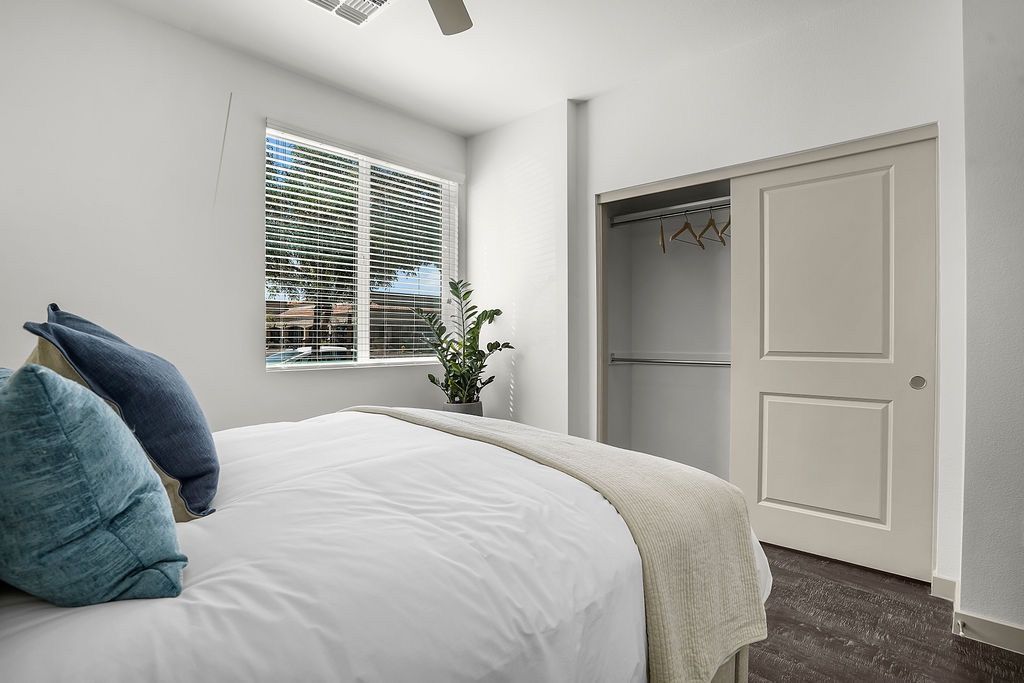 Bedroom in a modern apartment with a made bed, window blinds, and an open closet.
