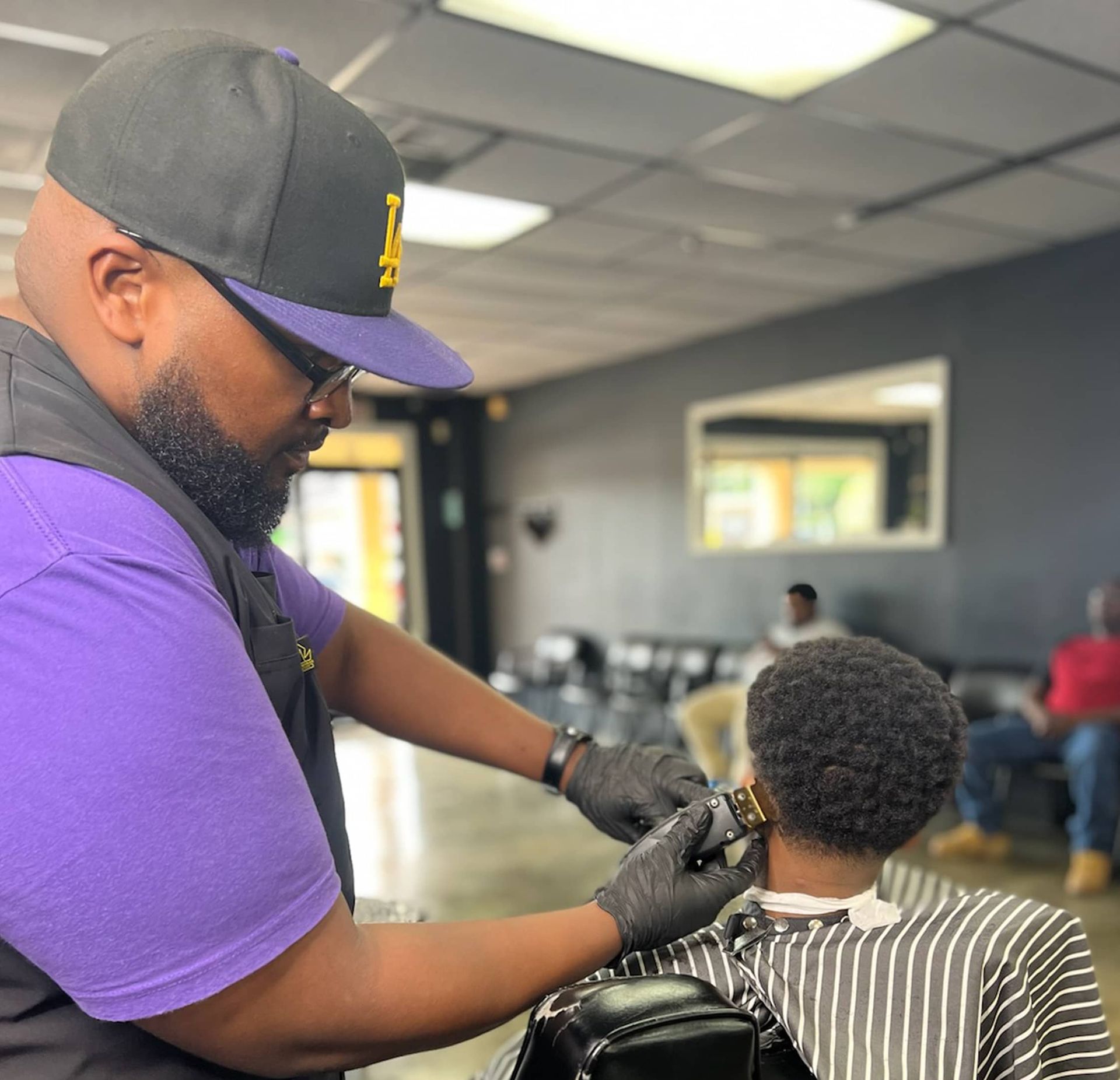 A man in a hat is cutting a man 's hair in a barber shop