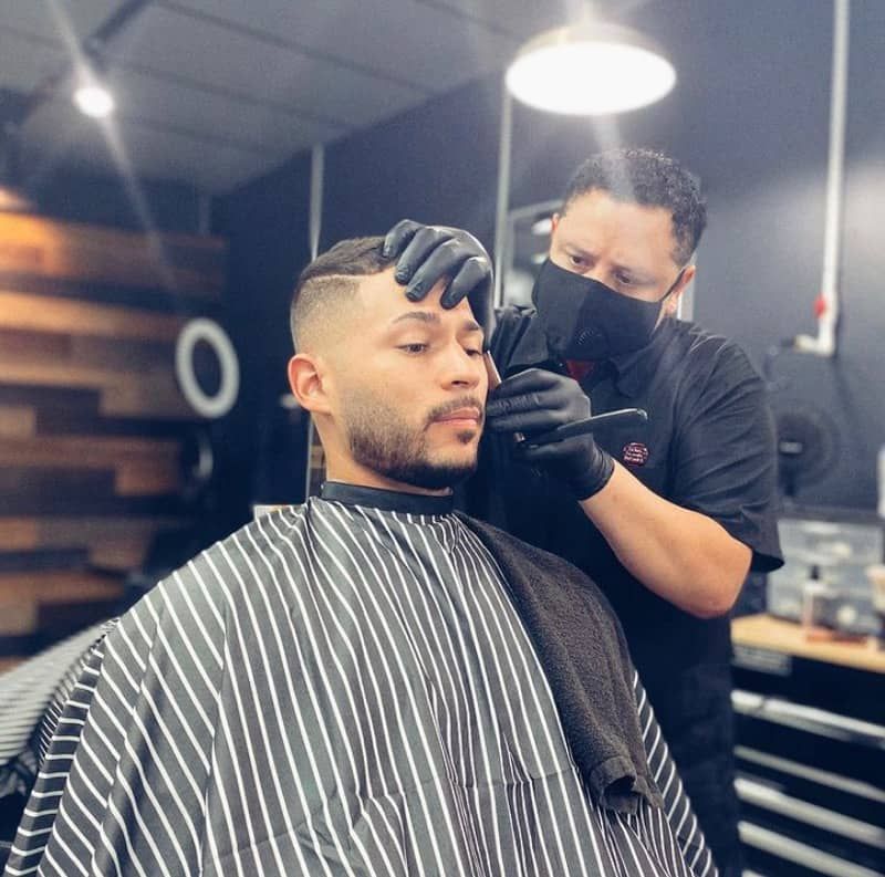 A man is getting his hair cut by a barber wearing a mask