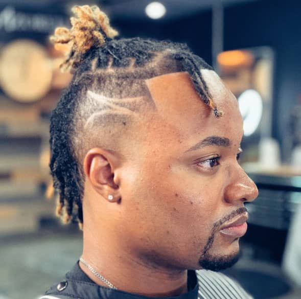 A man with dreadlocks and a beard is getting his hair cut by a barber.
