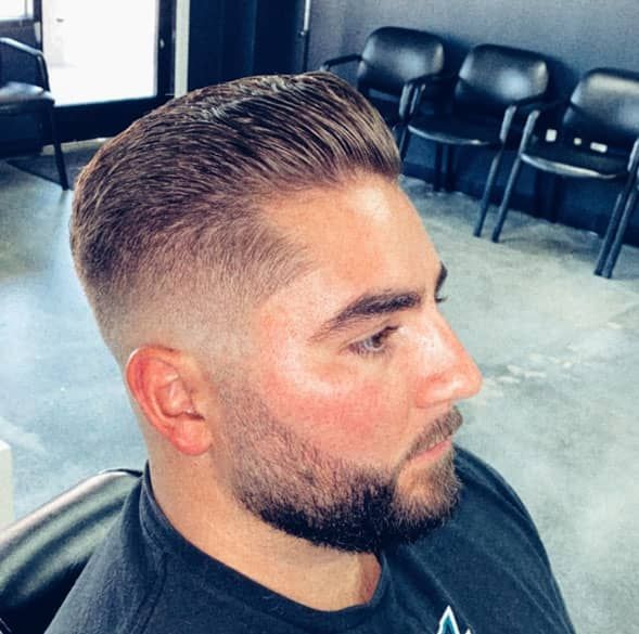 A man with a beard is sitting in a chair in a barber shop.