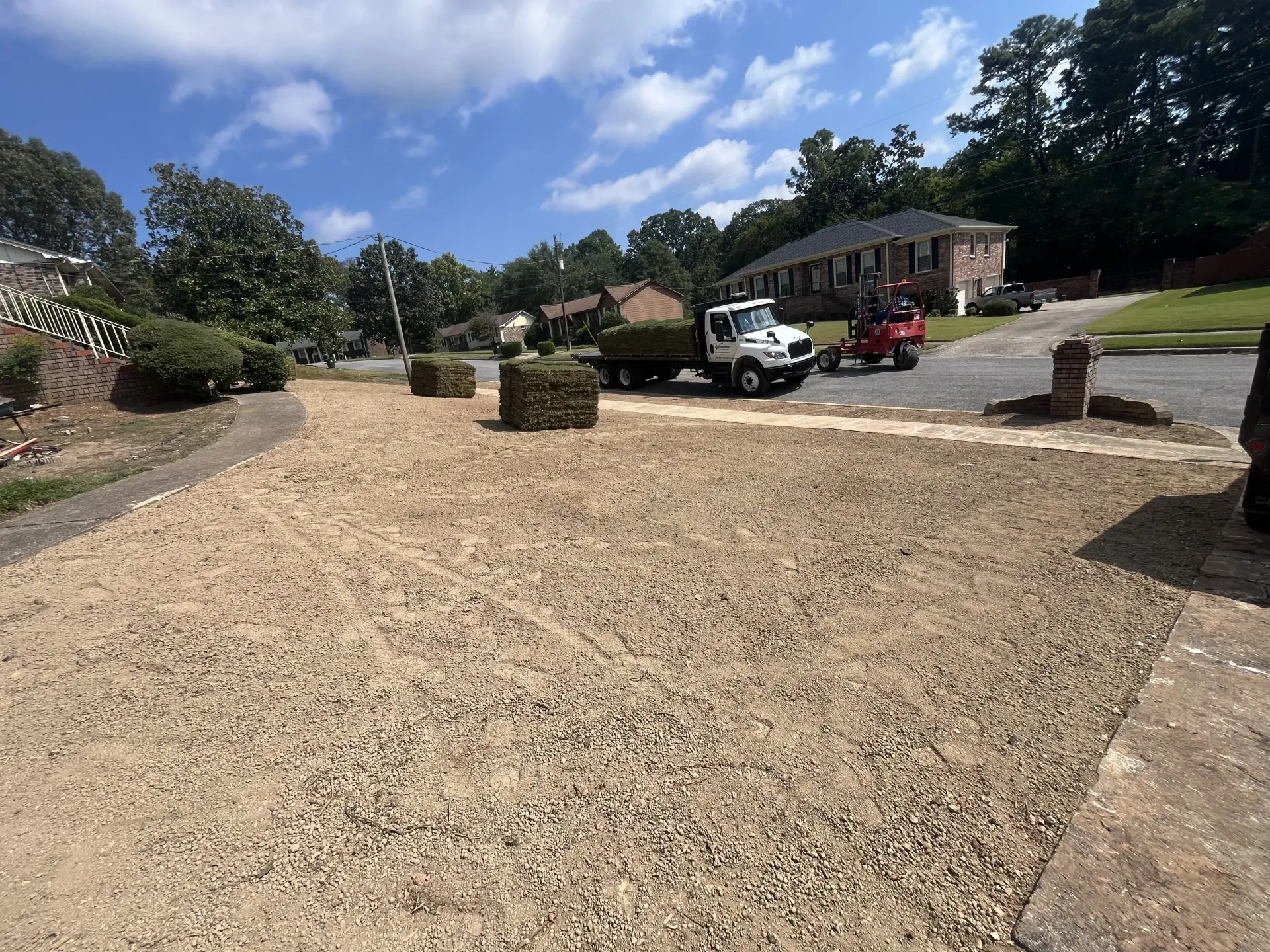 Gravel driveway with landscaping, parked trucks, and a house under a partly cloudy sky