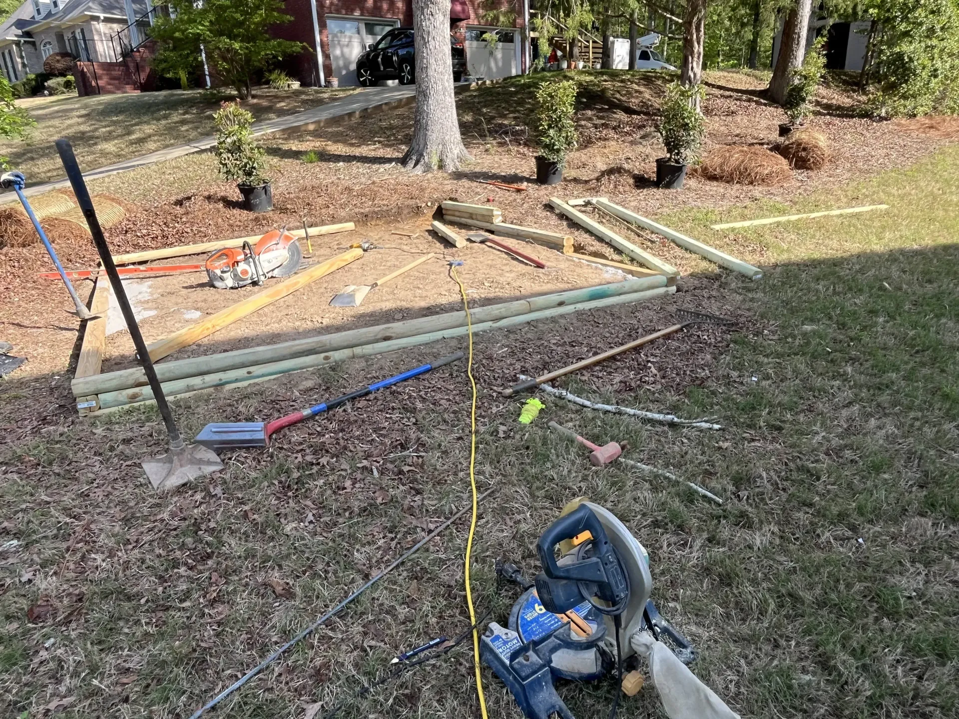 Partially framed backyard with tools, wood planks, and a chainsaw on the grass