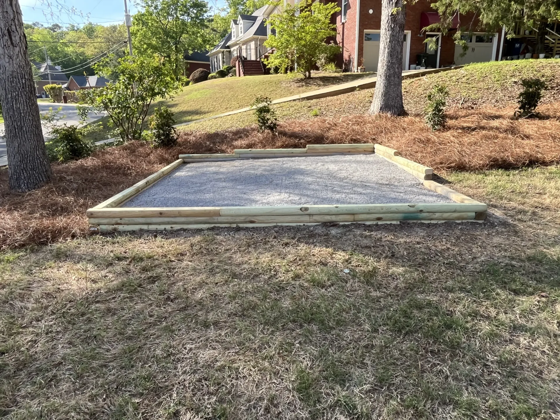 Raised wooden sandbox in a grassy front yard with trees and a house in the background