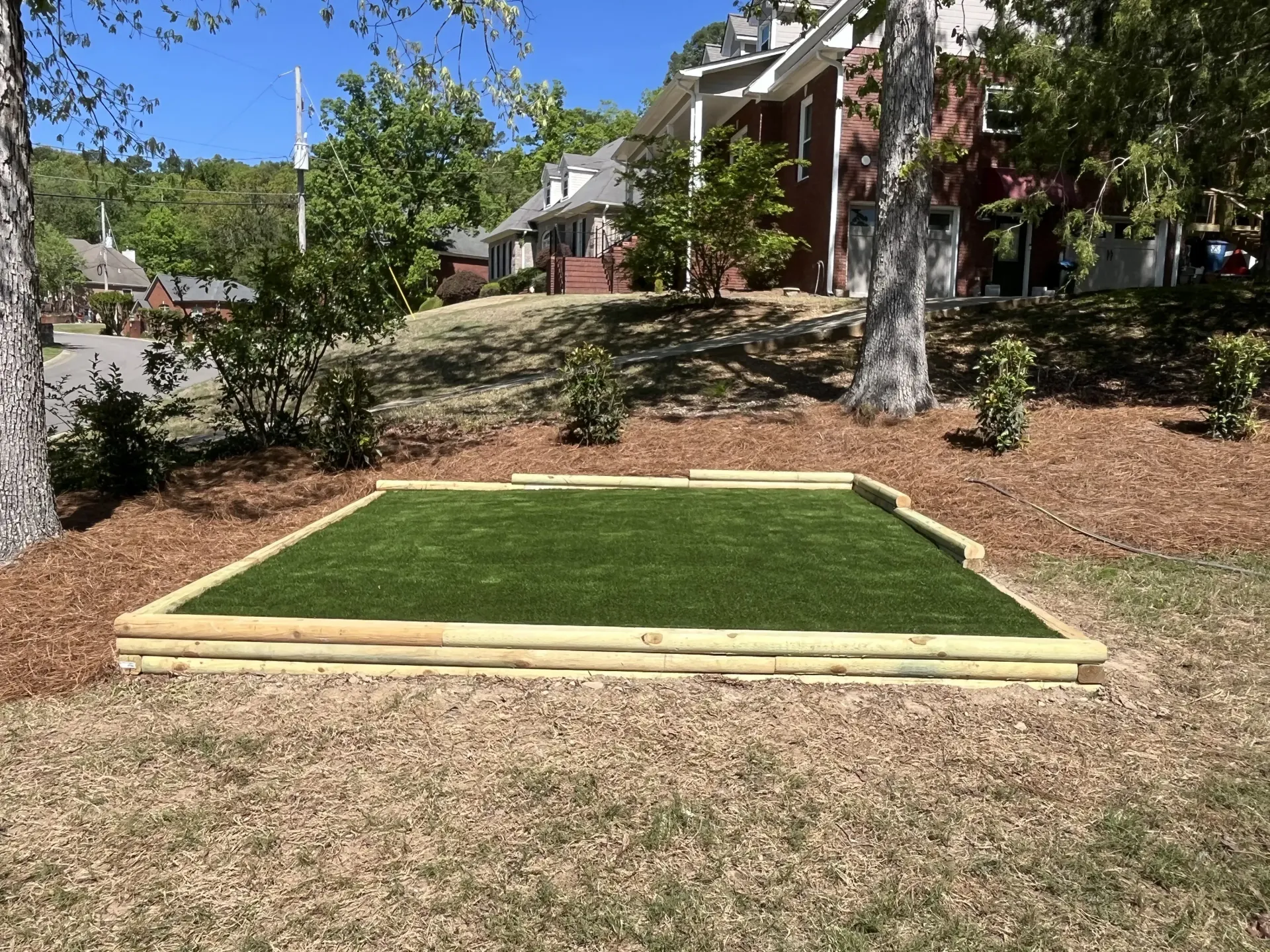 Freshly installed rectangular grass putting green in a landscaped yard under trees