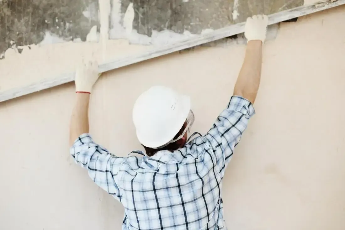 Worker in white hard hat inspecting a wall with arms raised
