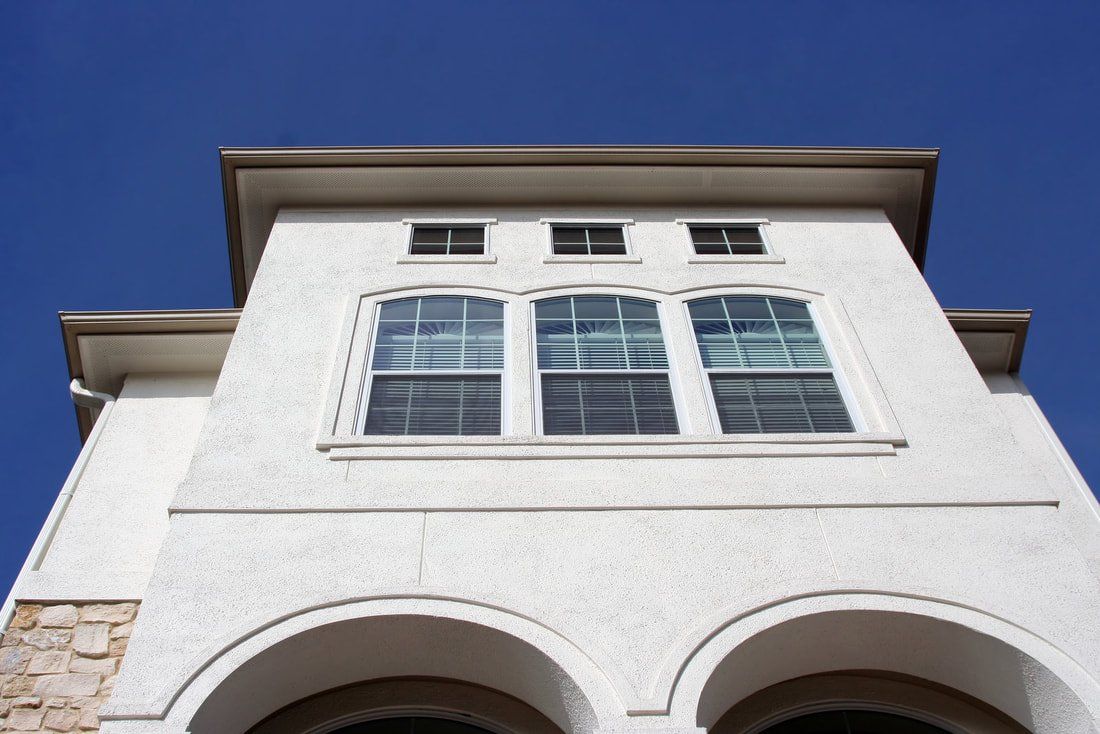 Low-angle view of a white stucco building with arched windows against a blue sky